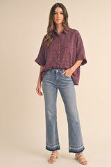 woman wearing a burgundy checkered oversized button-up shirt and light blue flared jeans with a hem detail