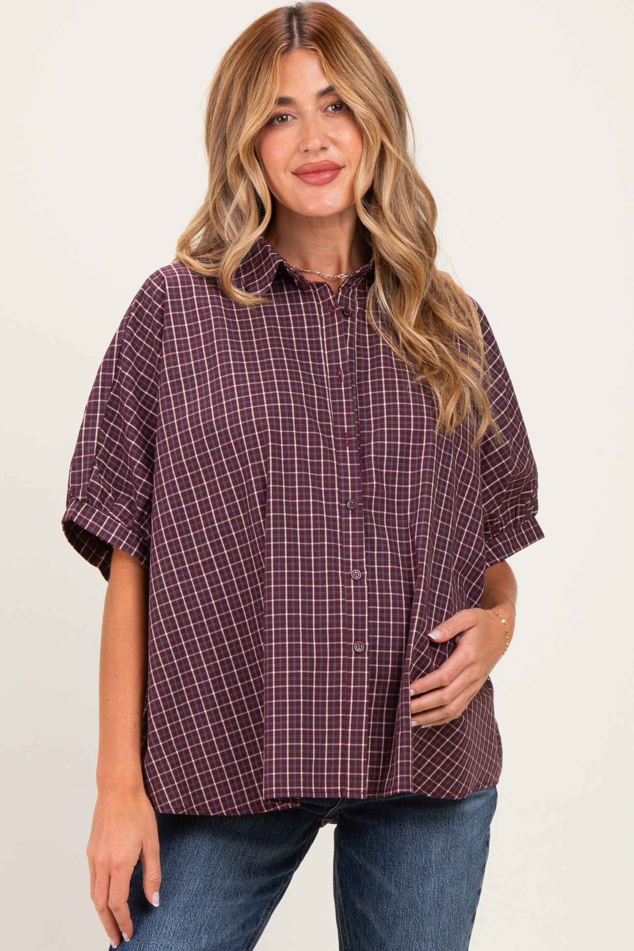 woman wearing a plum checkered maternity shirt with short sleeves and holding her baby bump