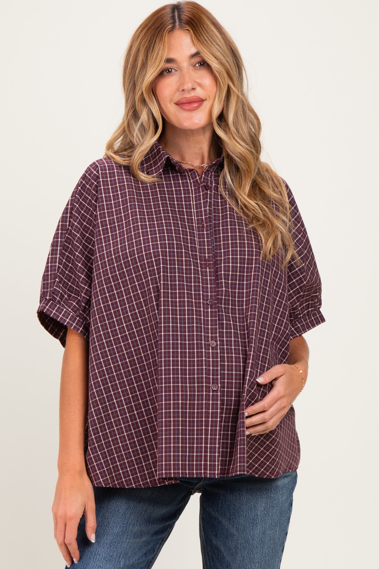 woman wearing a plum checkered maternity shirt with short sleeves and holding her baby bump