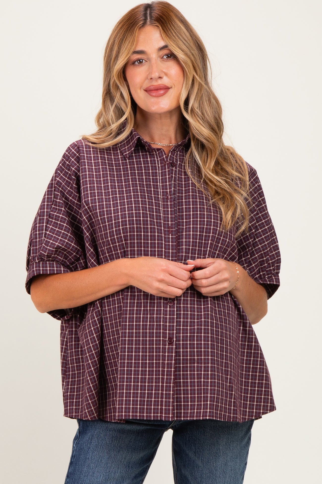 woman wearing a burgundy checkered maternity button-up shirt with a loose fit and rolled sleeves, holding her baby bump