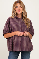 woman wearing a burgundy checkered maternity button-up shirt with a loose fit and rolled sleeves, holding her baby bump
