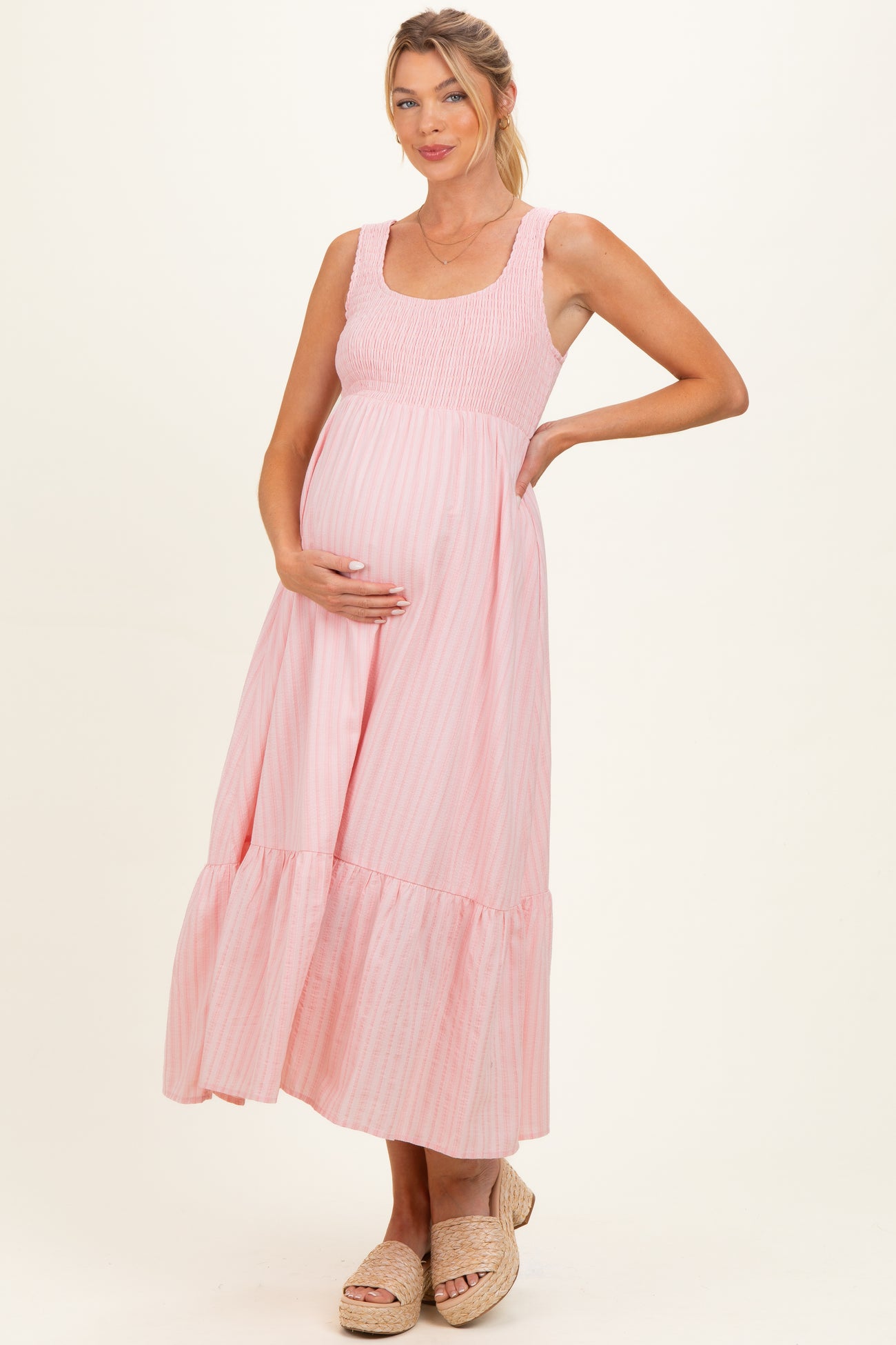 woman wearing a light pink striped maternity maxi dress with smocked bodice and ruffled hem, showing her baby bump