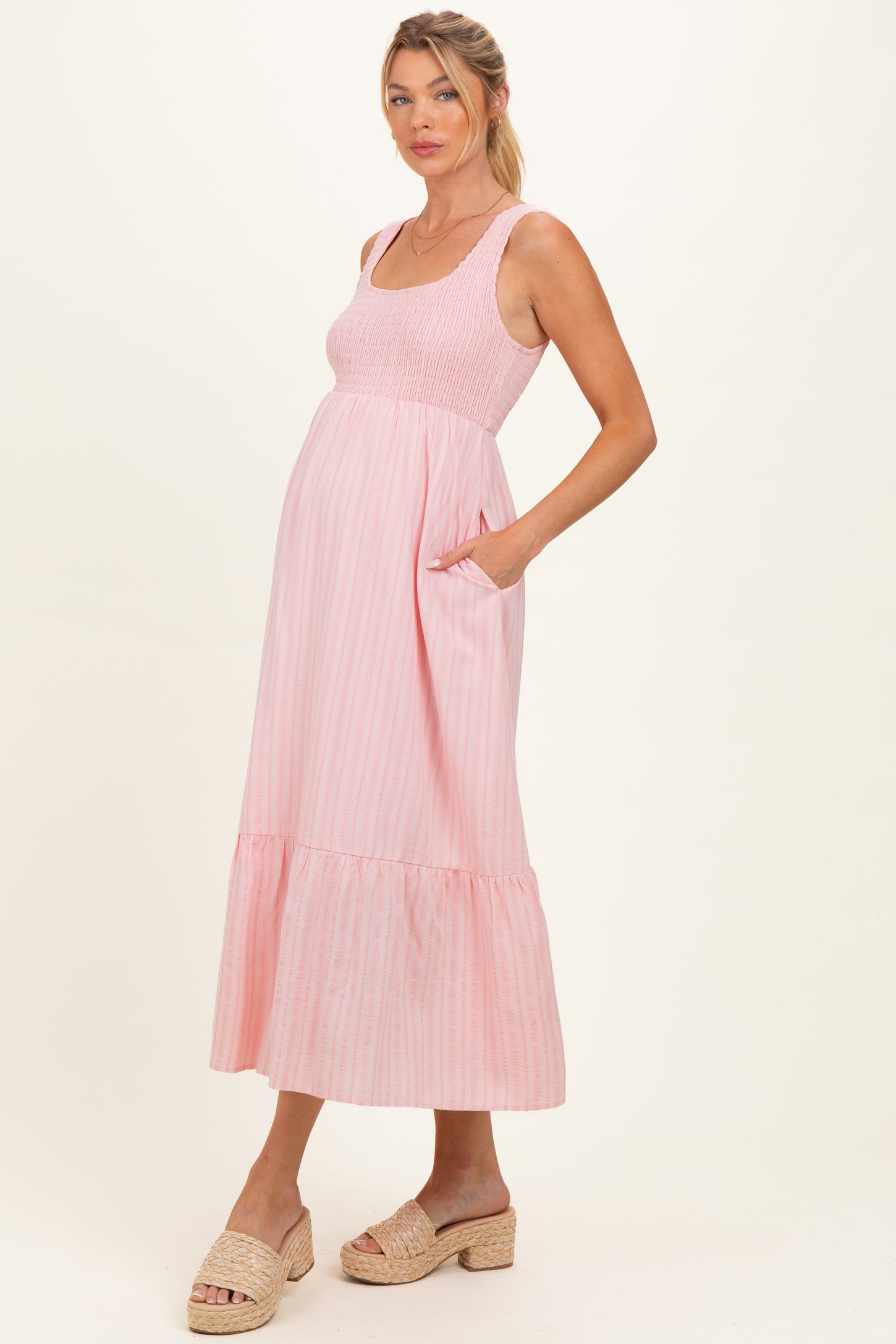 woman wearing a pink striped maternity dress with smocked bodice and ruffle hem, showing her baby bump