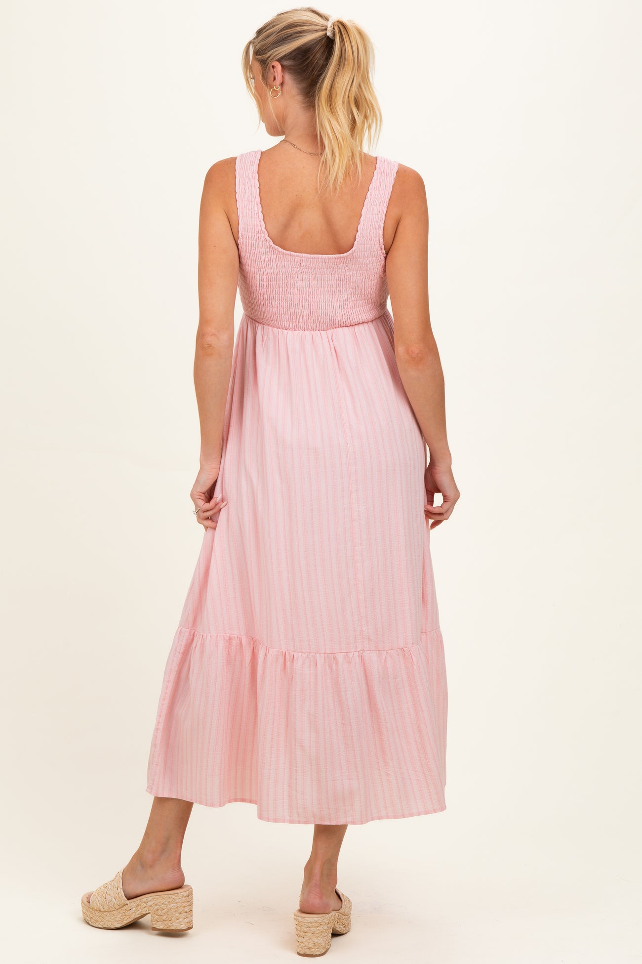 woman wearing a pink striped maternity maxi dress with a smocked bodice and tiered skirt, showing her baby bump