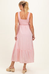 woman wearing a pink striped maternity maxi dress with a smocked bodice and tiered skirt, showing her baby bump