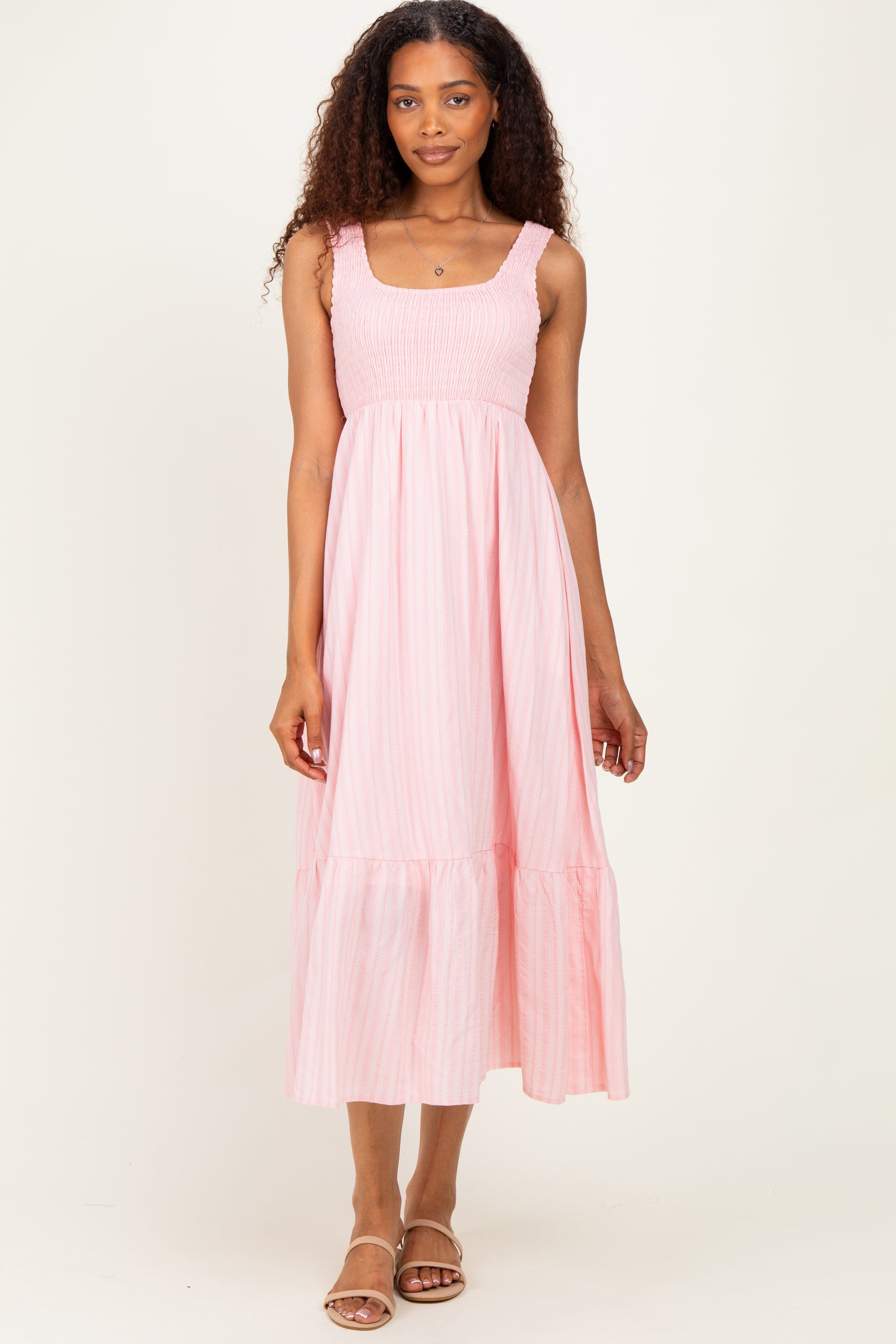 woman wearing a pink striped maxi dress with a smocked bodice and tiered skirt, standing on a neutral background