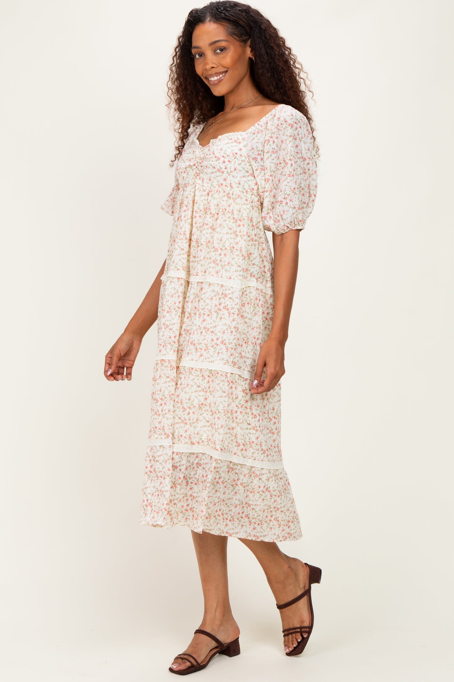 woman wearing a floral print midi dress with puff sleeves and a tiered skirt, smiling against a neutral background
