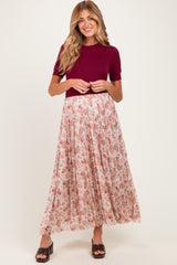 woman wearing a burgundy short sleeve top and a flowy floral maternity skirt with a pleated design
