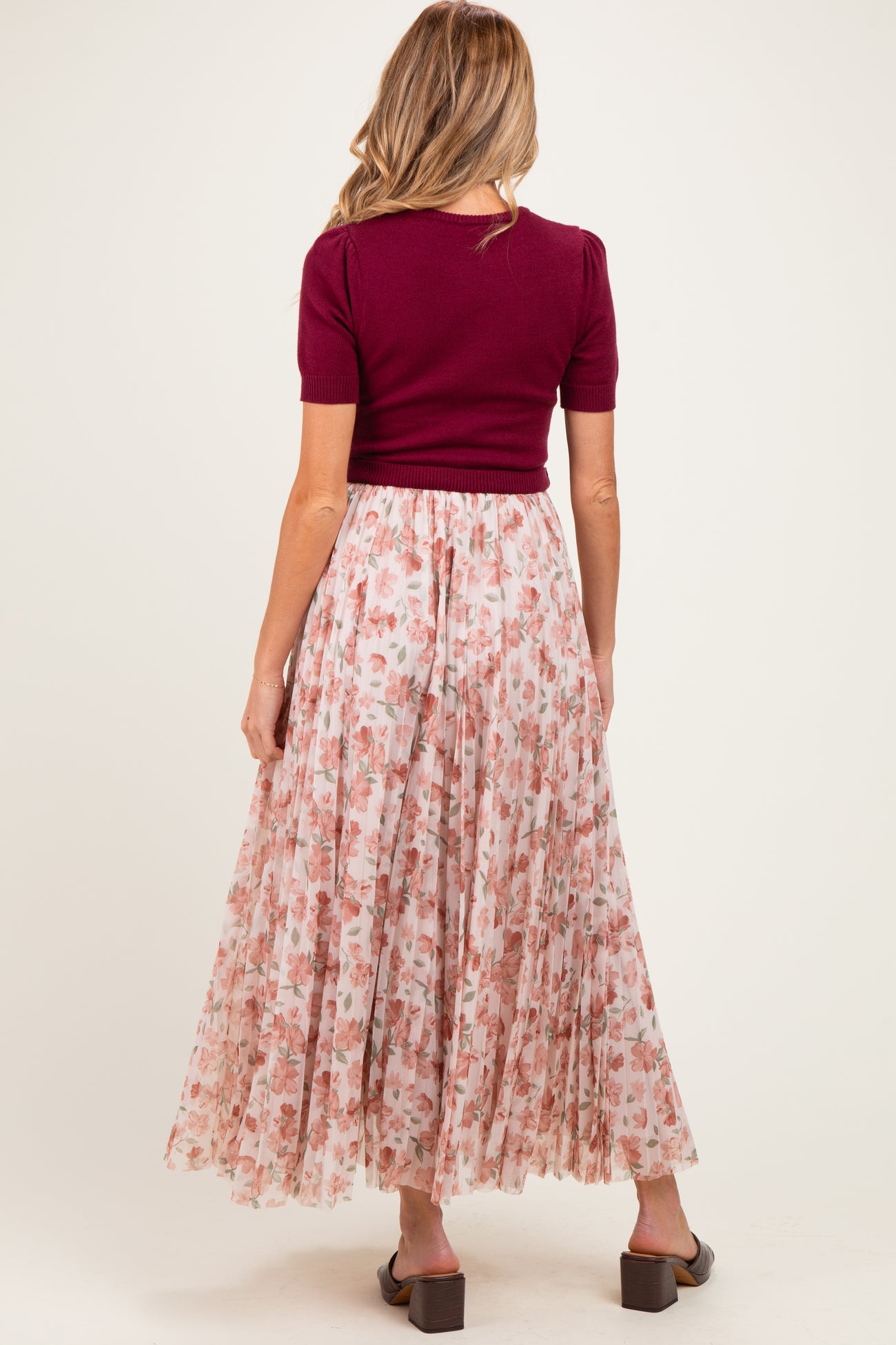 woman wearing a maroon short sleeve top and a flowy pink floral maternity skirt from the back