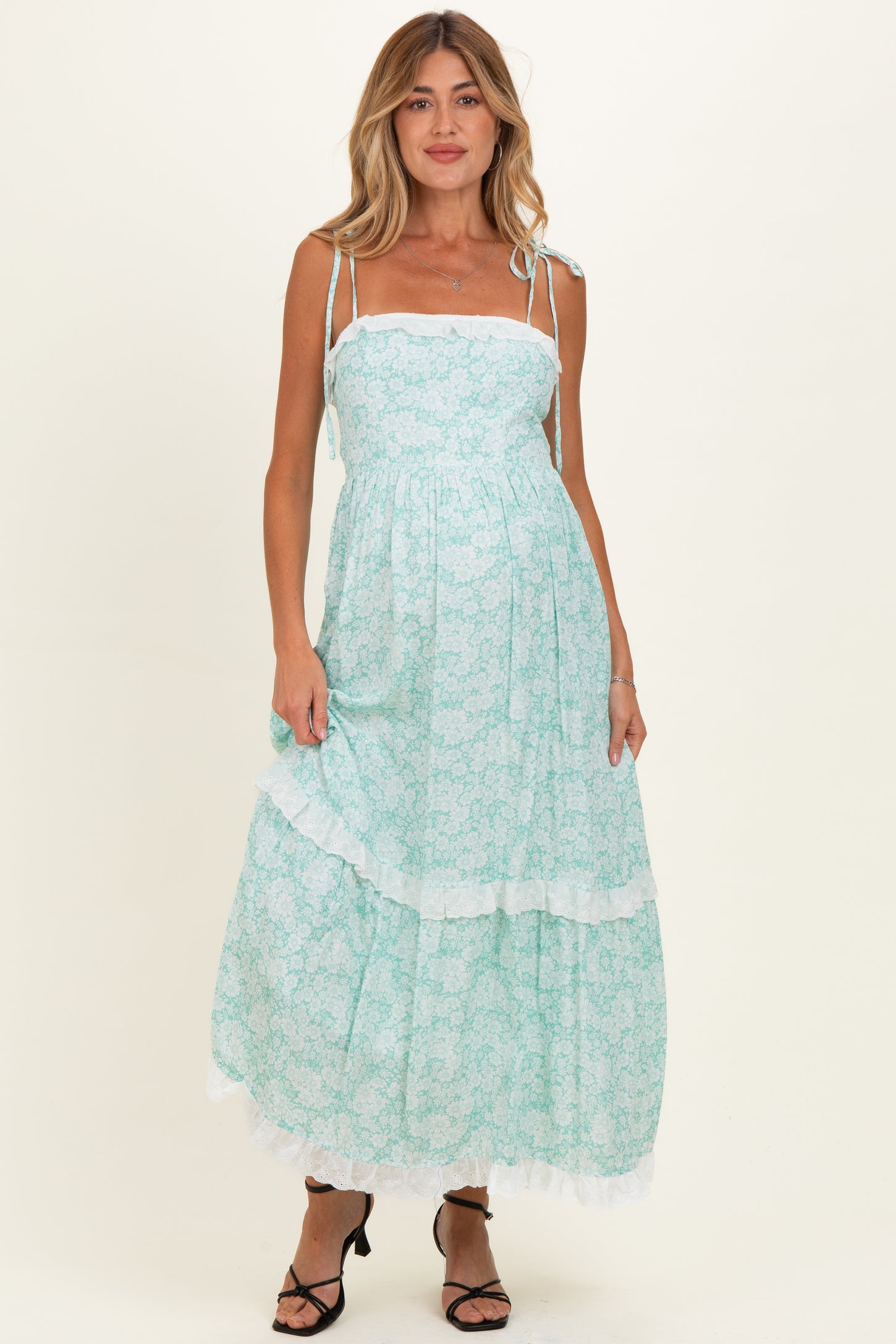 woman wearing a mint green floral maternity maxi dress with adjustable straps and ruffled hem