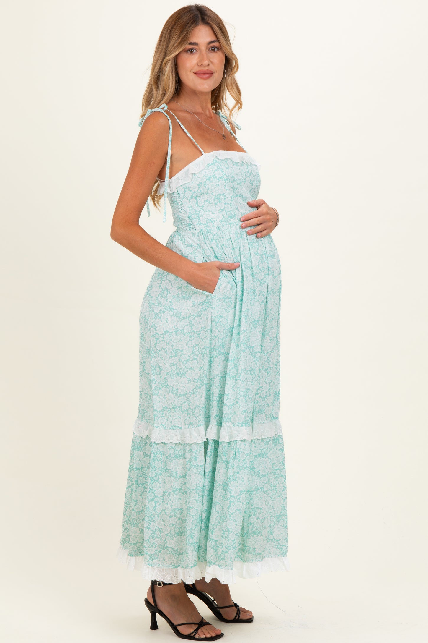 woman wearing a mint green maternity maxi dress with a floral print, adjustable straps, and a baby bump visible