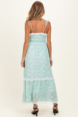 woman wearing a light green floral maternity maxi dress with adjustable straps and a ruffled hem, showing her back