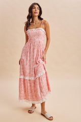 woman wearing a pink floral maxi dress with lace trim and spaghetti straps, standing on a beige background