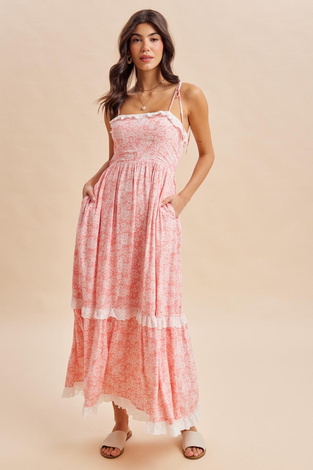 woman wearing a pink floral maxi dress with spaghetti straps and ruffle details, standing and posing confidently