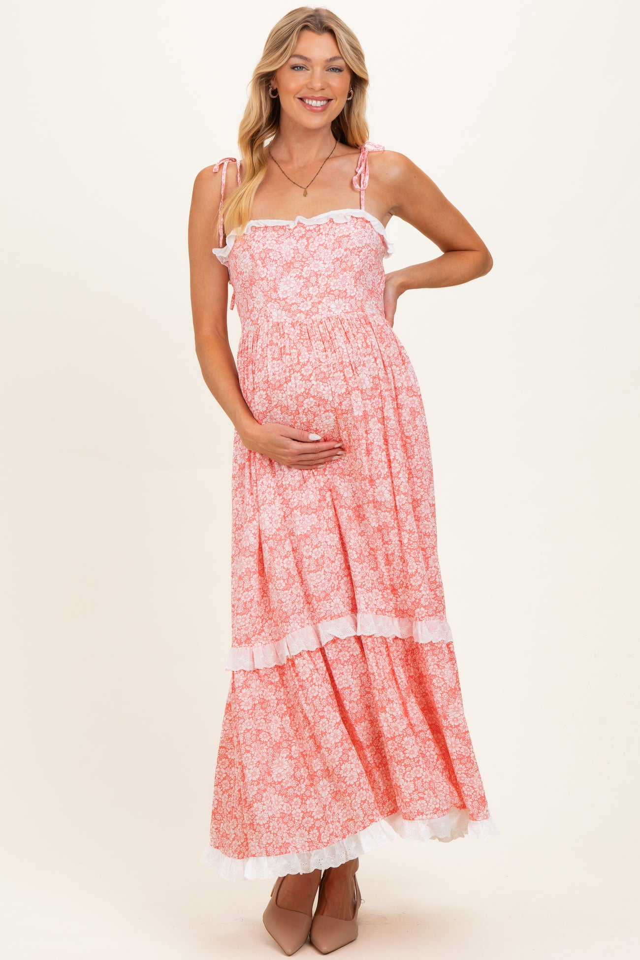 woman wearing a pink floral maternity maxi dress with ruffled straps and holding her baby bump