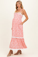woman wearing a pink floral maternity maxi dress with lace trim and pockets, showcasing her baby bump