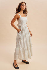woman wearing a white polka dot maxi dress with square neckline and tie back detail, standing in a relaxed pose