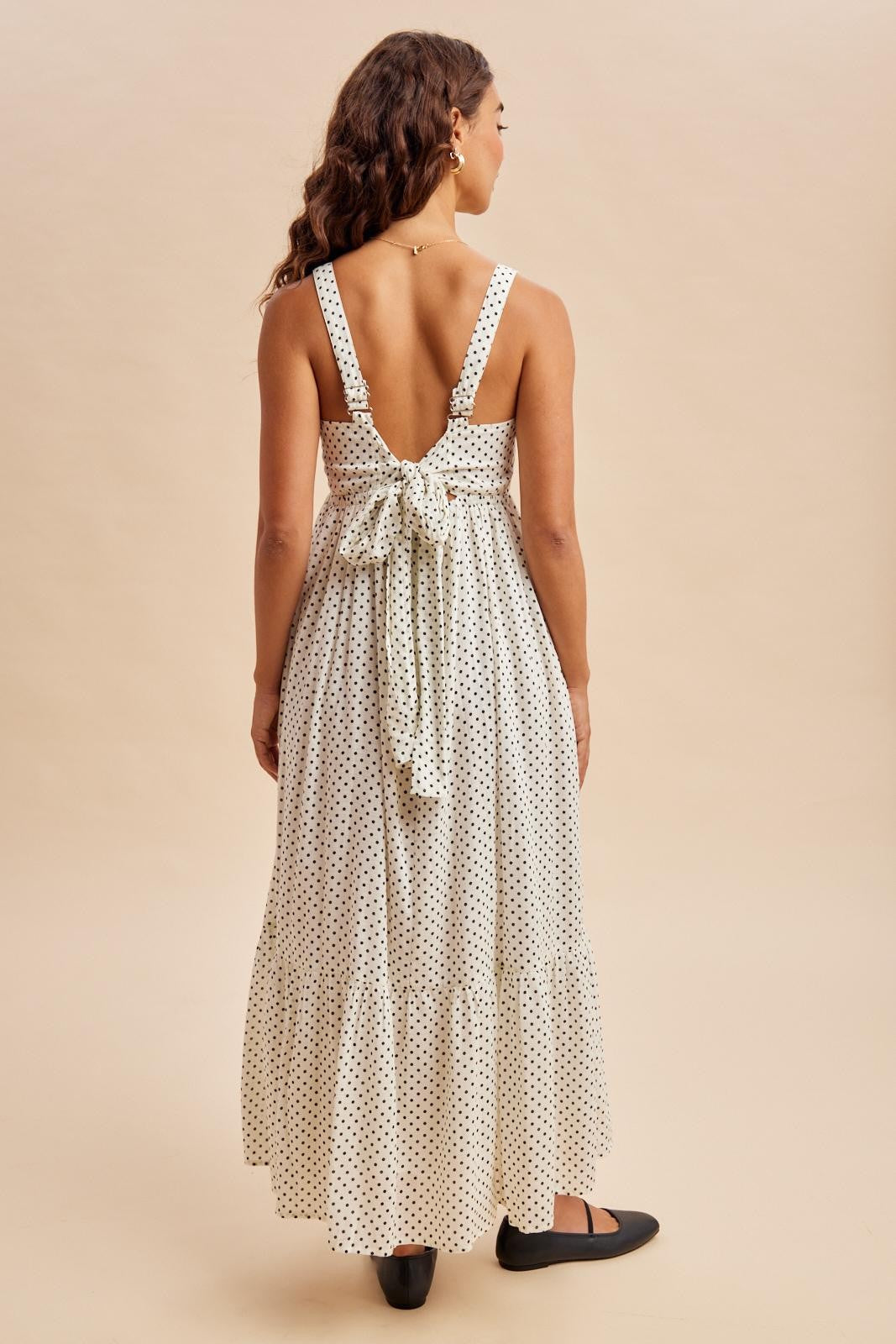 woman wearing a white polka dot maxi dress with a back tie detail and a tiered hem, viewed from the back