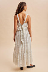 woman wearing a white polka dot maxi dress with a back tie detail and a tiered hem, viewed from the back
