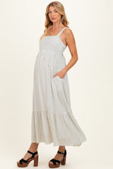 woman wearing a white polka dot maternity dress with a tiered skirt and pockets, standing in platform sandals