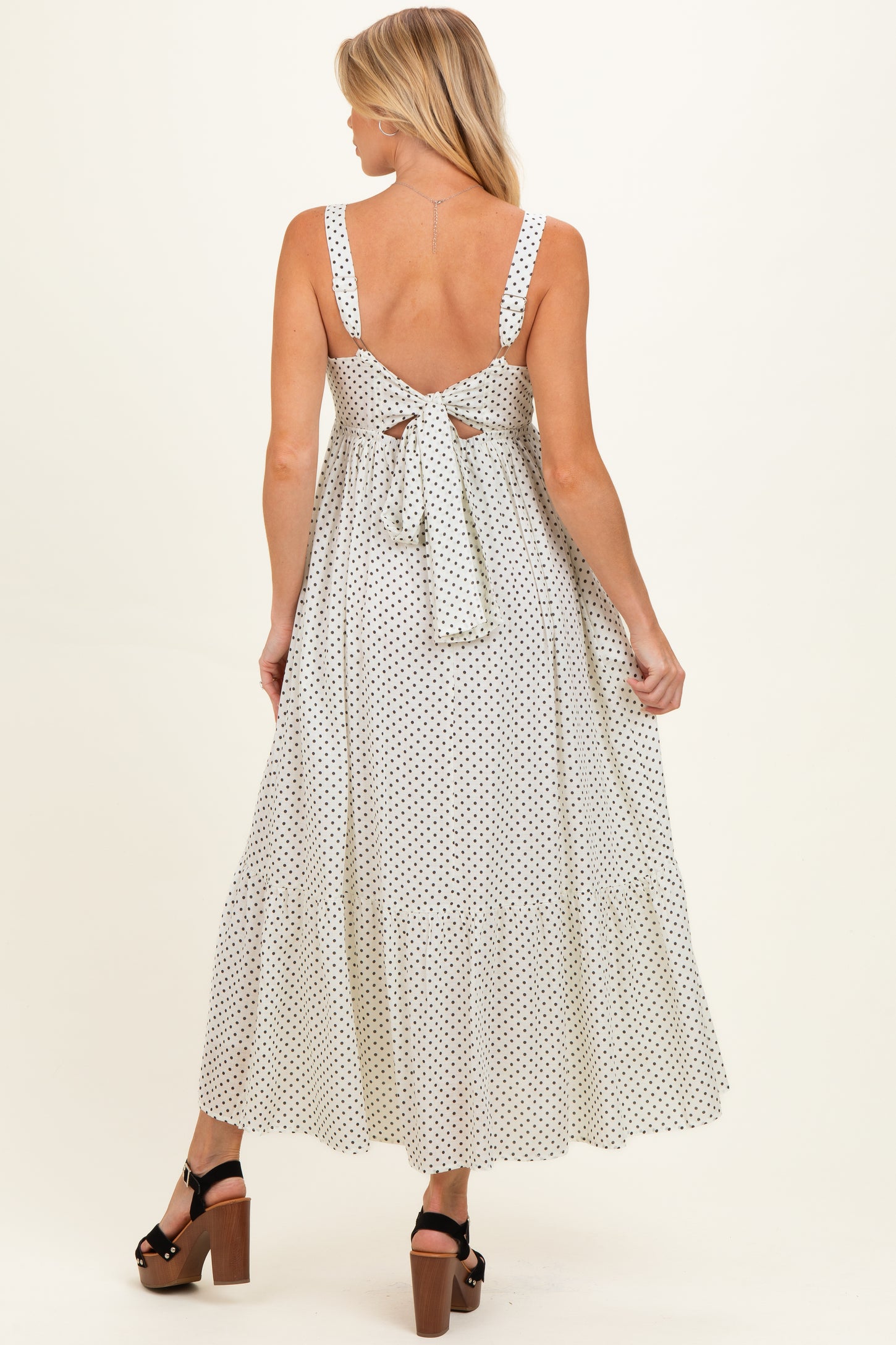 woman wearing a white polka dot maternity maxi dress with back tie detail and a flared skirt, showing baby bump