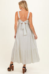 woman wearing a white polka dot maternity maxi dress with back tie detail and a flared skirt, showing baby bump