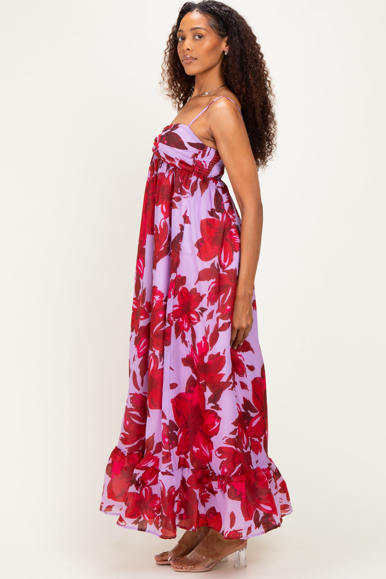 woman wearing a sleeveless purple maxi dress with red floral print and ruffled hem