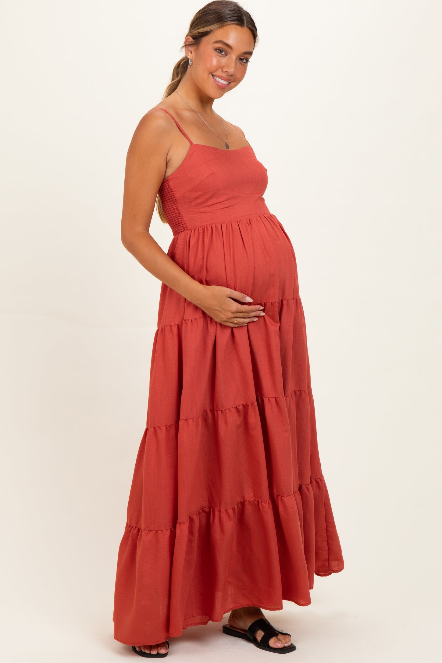 woman wearing a rust-colored maternity maxi dress with tiered skirt, holding her baby bump