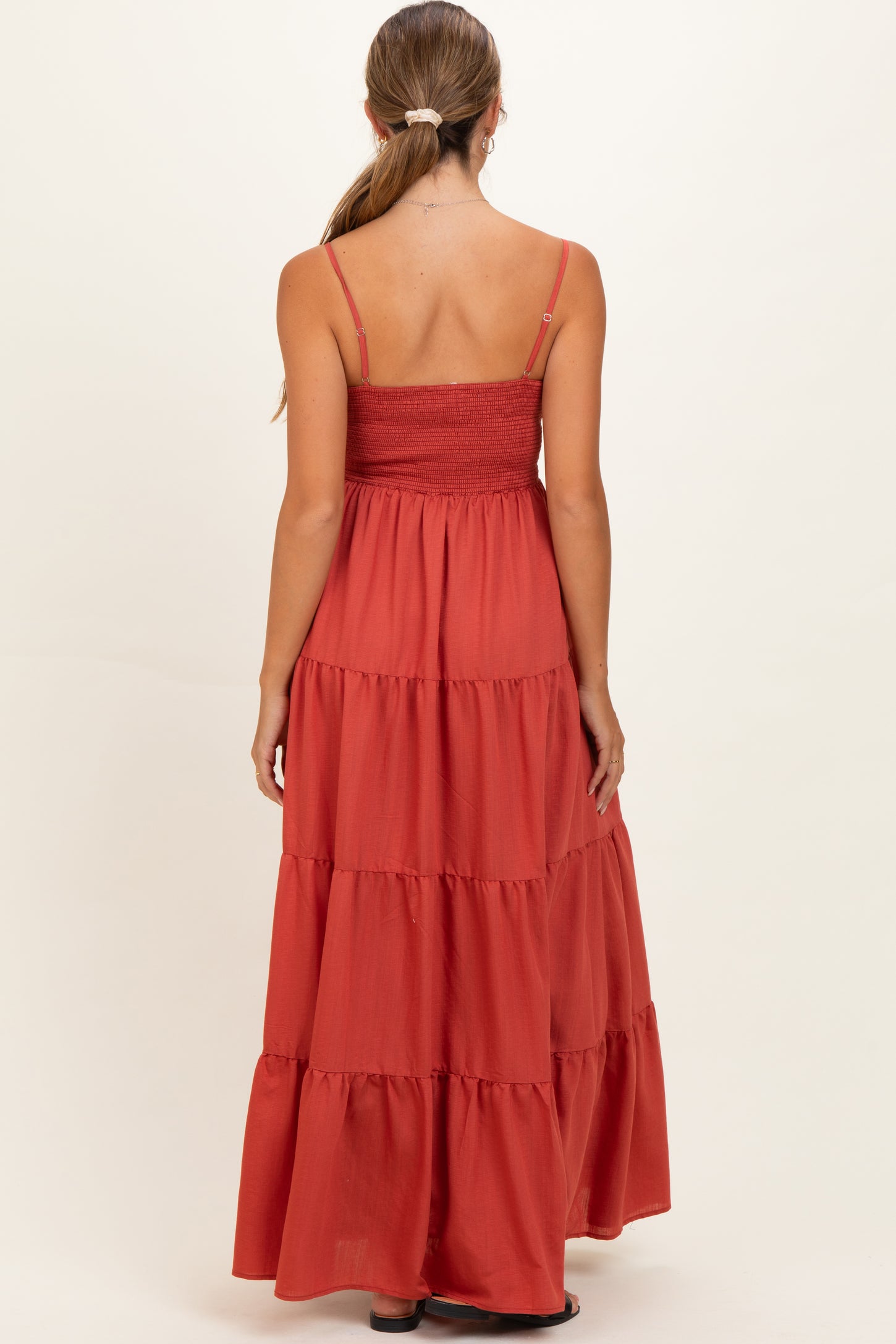 woman wearing a rust red maternity maxi dress with tiered ruffles and thin straps, showing her back