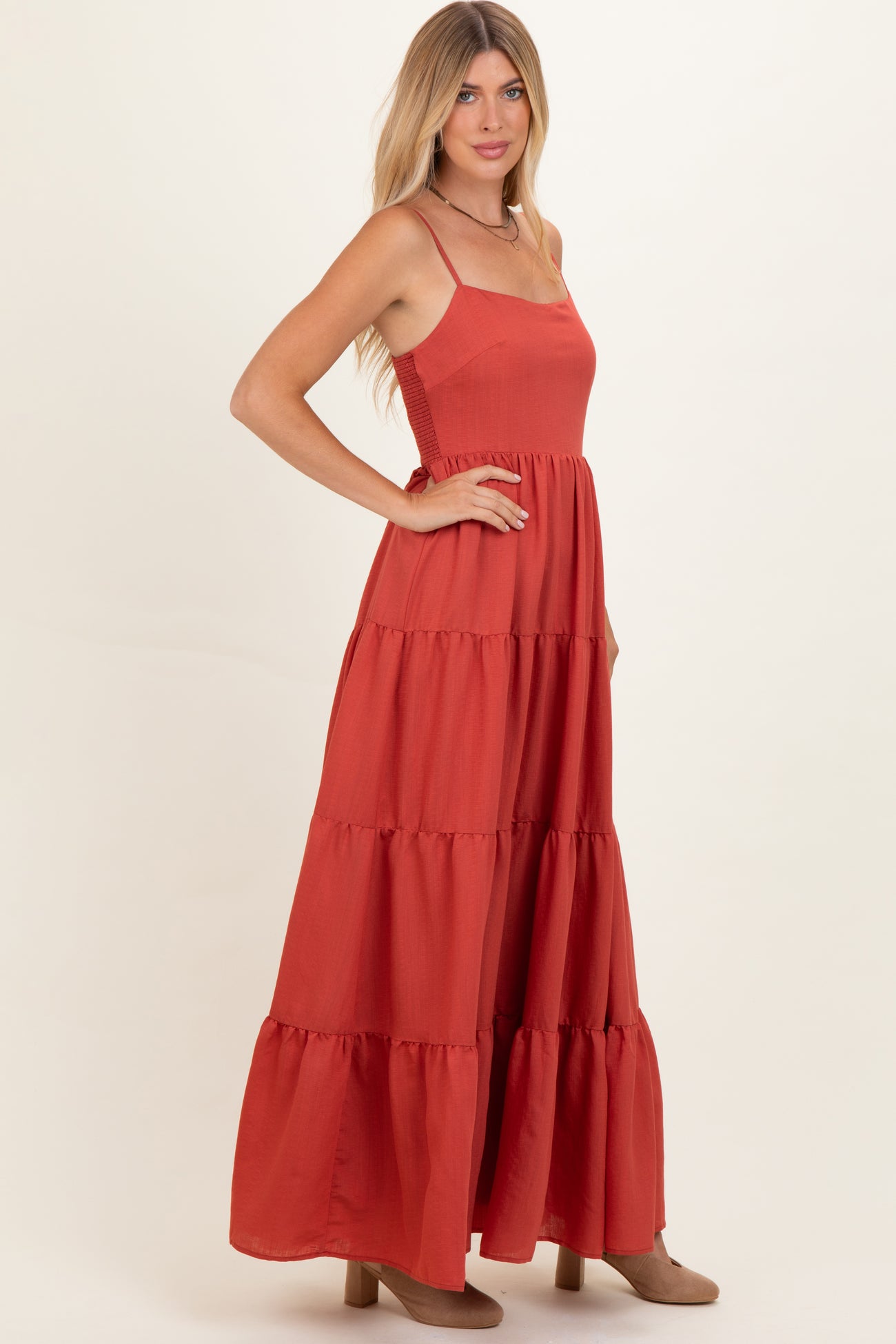 woman wearing a rust-colored maxi dress with a tiered design and spaghetti straps