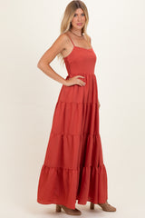 woman wearing a rust-colored maxi dress with a tiered design and spaghetti straps