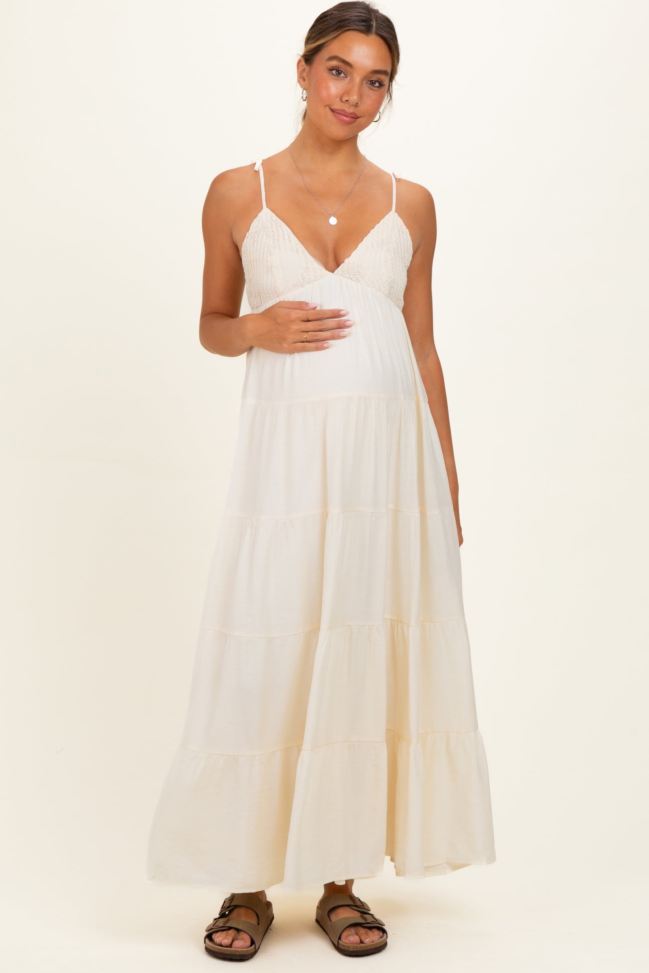 woman wearing a cream maternity maxi dress with a tiered design and holding her baby bump