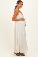 woman wearing a cream tiered maternity maxi dress with a fitted bodice, holding her baby bump