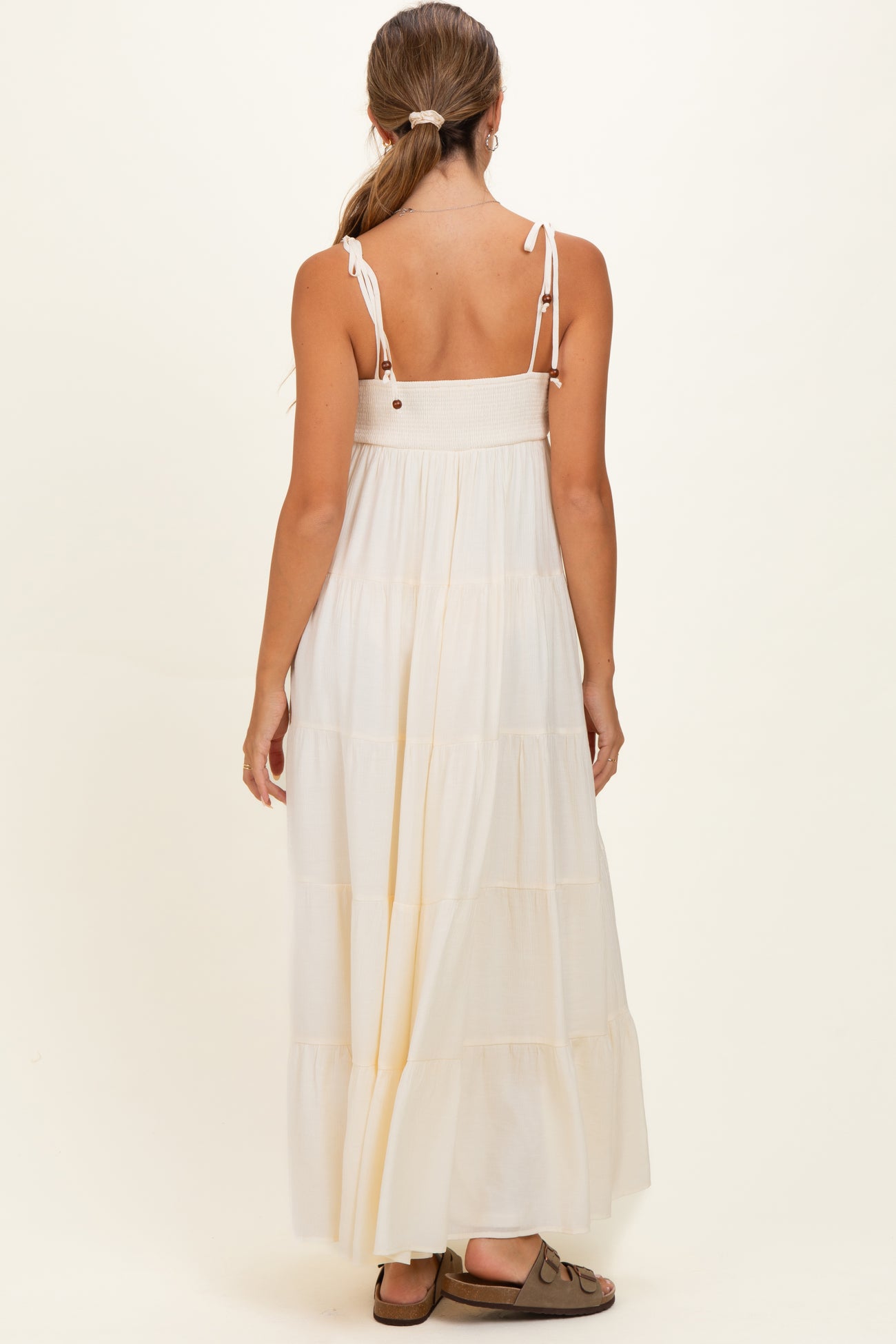 woman wearing a white tiered maxi maternity dress with adjustable straps and a smocked bodice, showing her back
