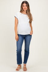 woman wearing a white maternity top with navy trim and blue jeans, showing her baby bump