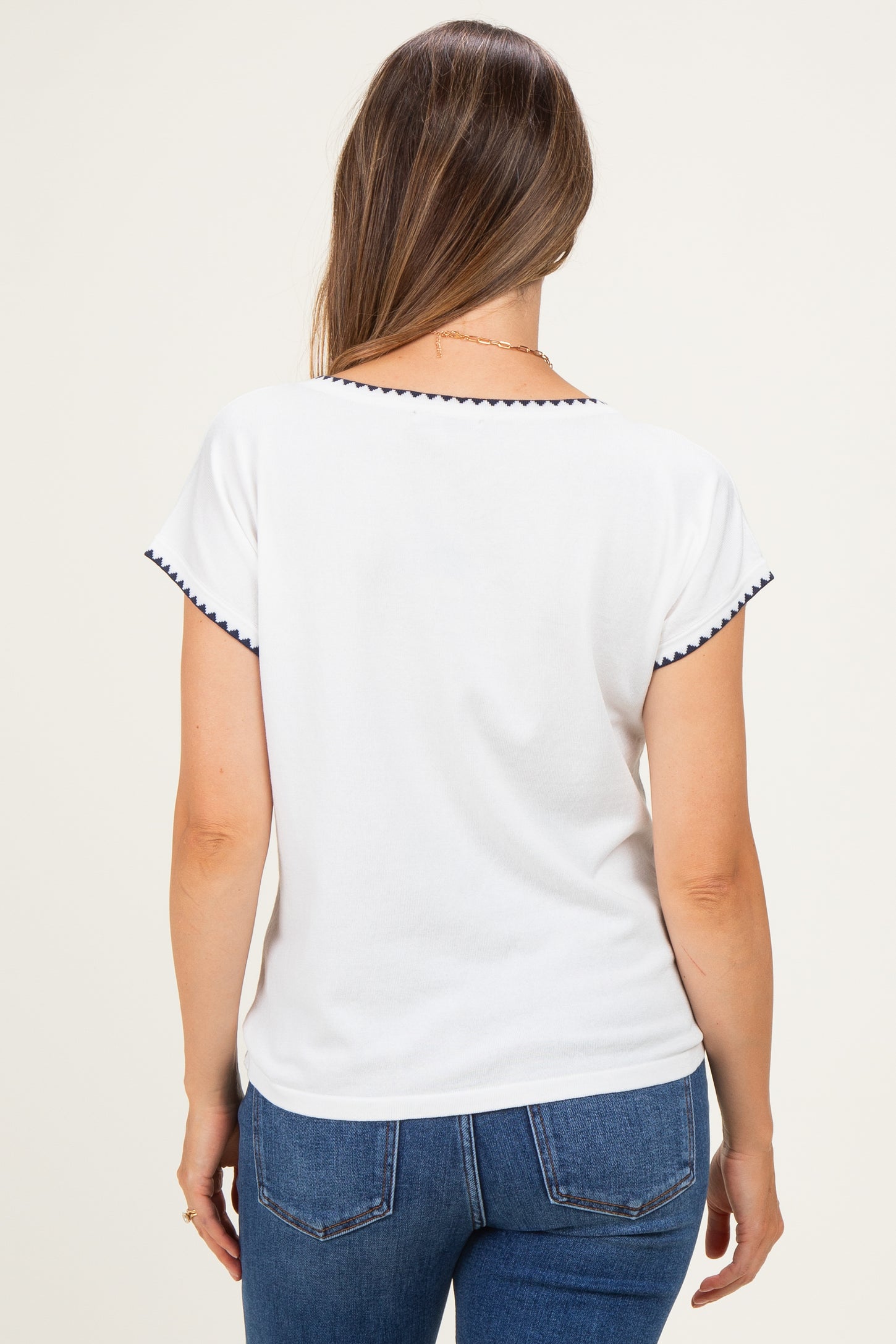 woman wearing a white maternity top with navy trim on the sleeves, seen from the back