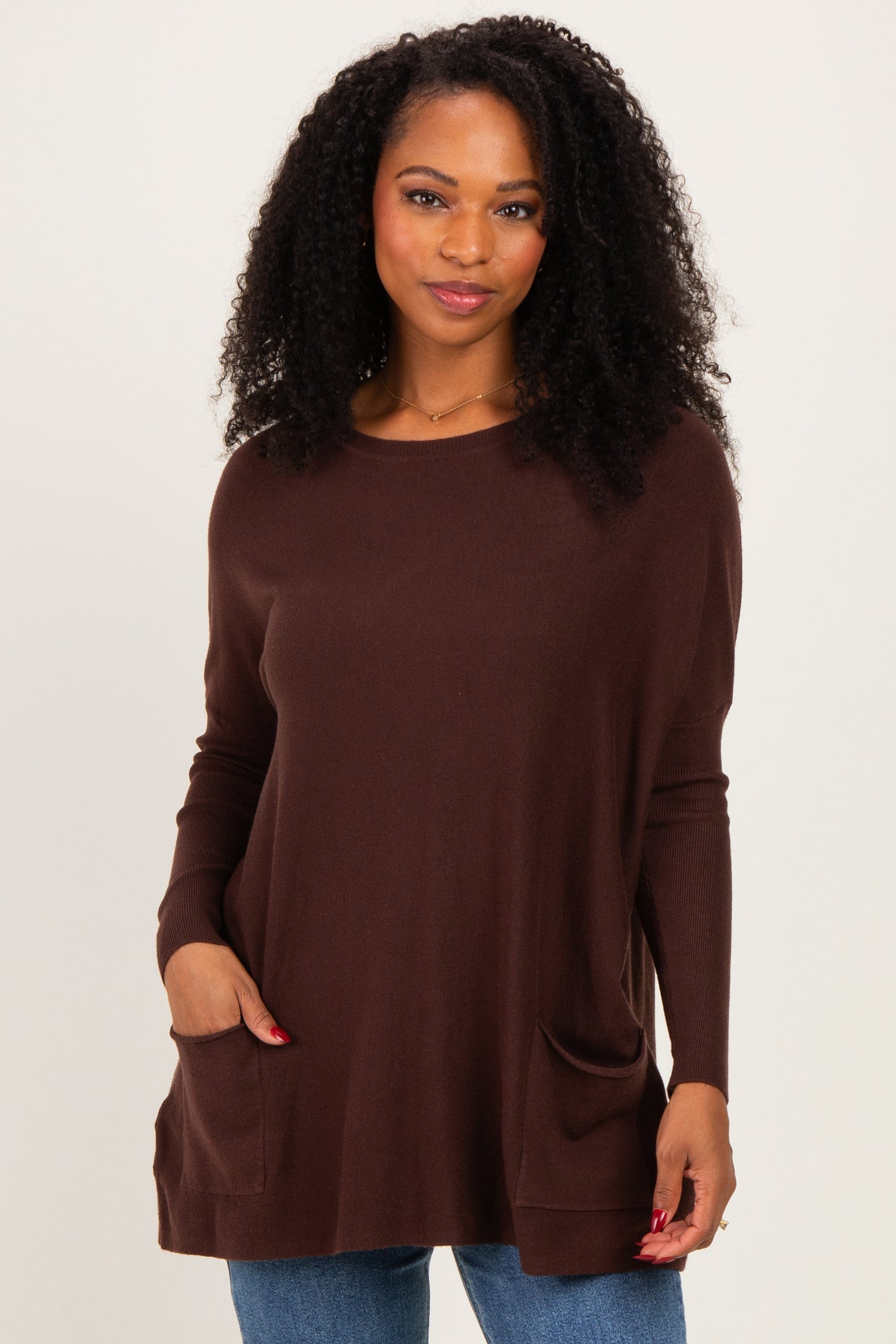 woman wearing a dark brown knit top with side pockets and long sleeves, standing against a light background