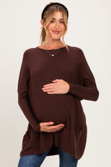 woman wearing a brown long sleeve maternity sweater with pockets and holding her baby bump