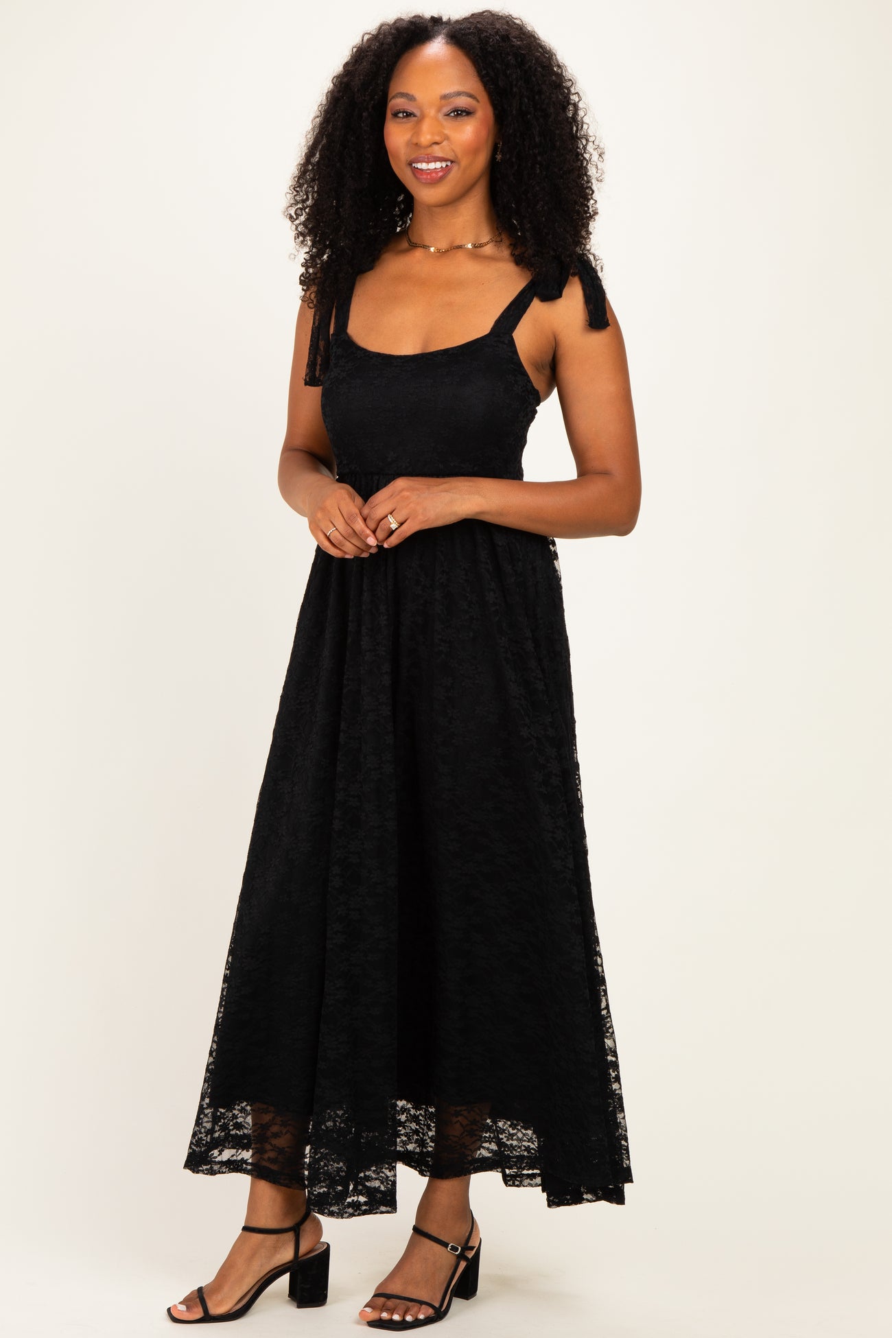 woman wearing a black lace maxi dress with tie straps and a flowing skirt, standing against a neutral background