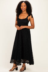 woman wearing a black lace maxi dress with tie straps and a flowing skirt, standing against a neutral background