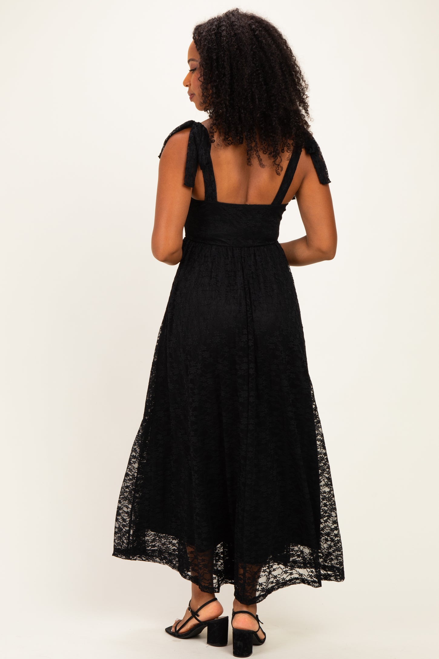 woman wearing a black lace maxi dress with tie shoulder straps and a fitted waist, viewed from the back