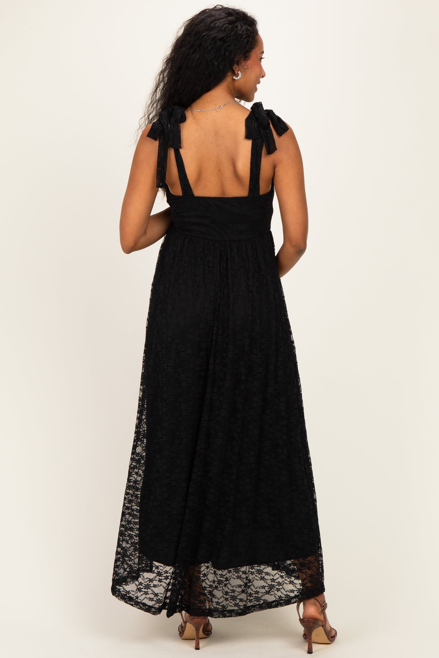 woman wearing a black lace maternity maxi dress with bow-tie shoulder straps, showing a relaxed fit and back detail