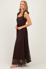 woman wearing a brown lace maxi dress with shoulder ties and a fitted bodice, standing sideways with a smile