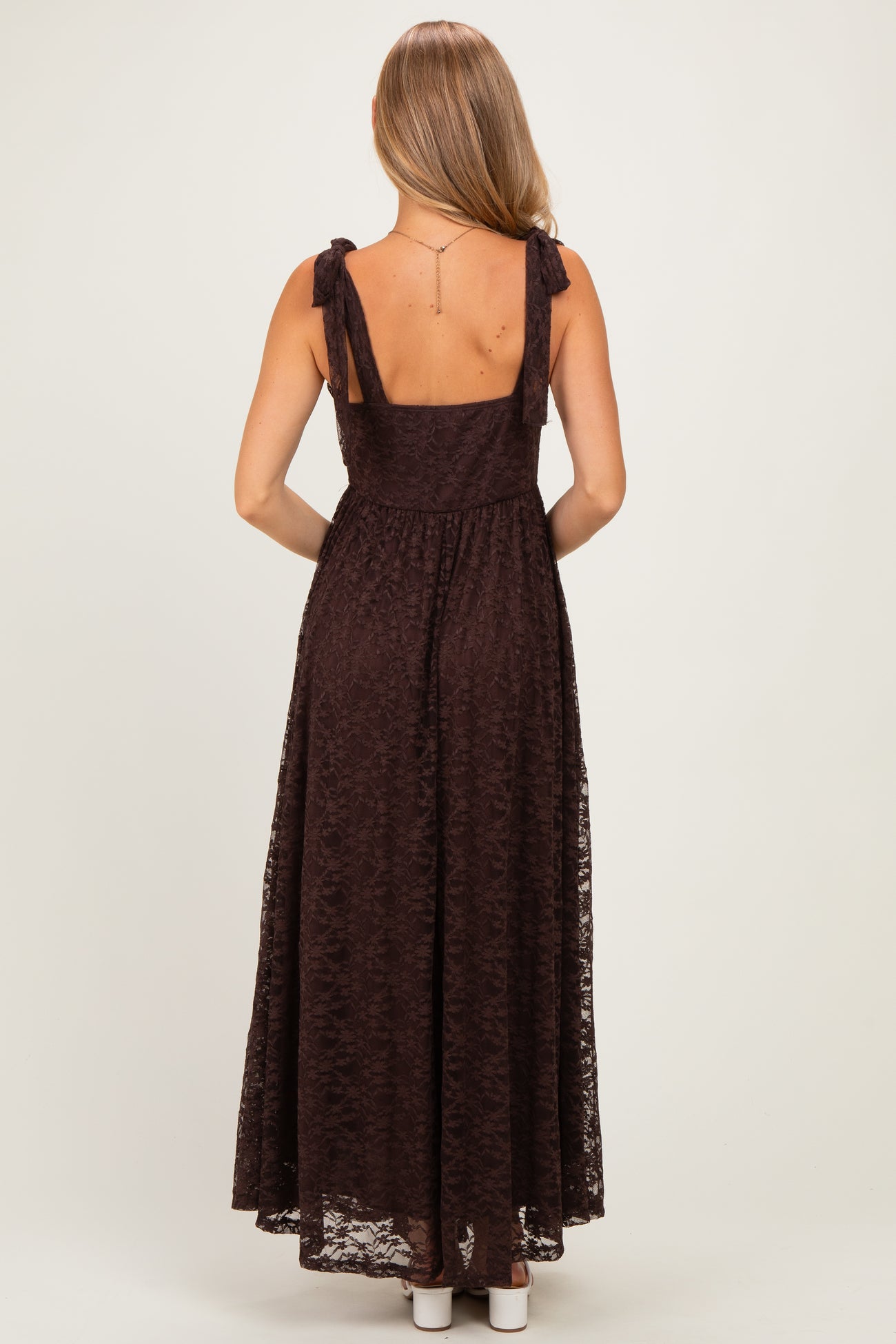woman wearing a burgundy maxi dress with tie straps and lace overlay, viewed from the back