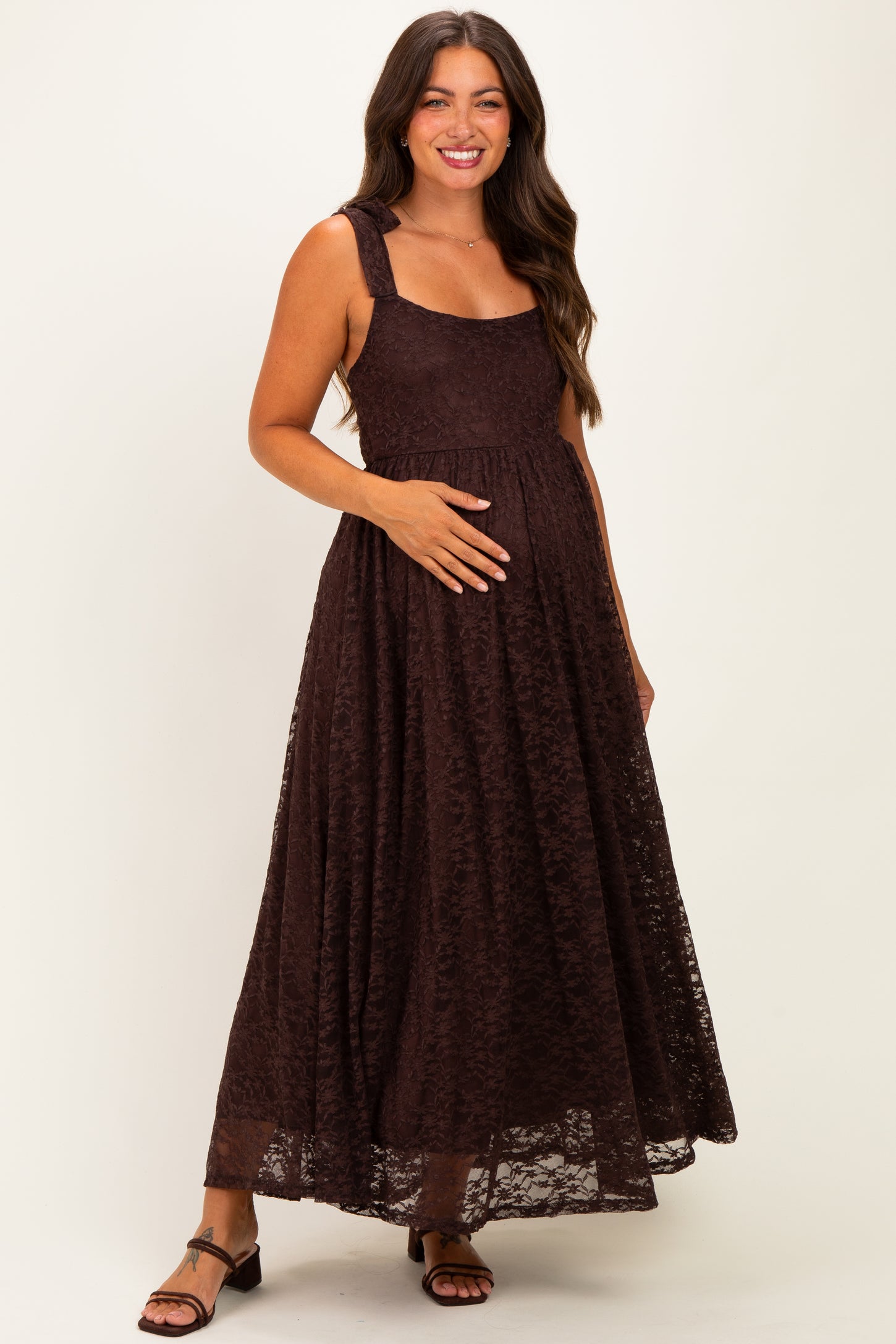 woman wearing a dark brown lace maternity dress and holding her baby bump