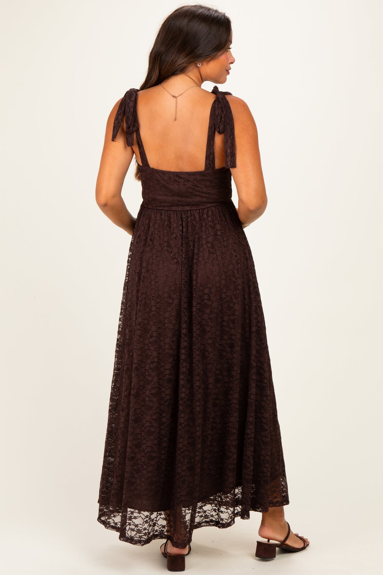 woman wearing a brown lace maternity maxi dress with tie straps, showing a baby bump from the back