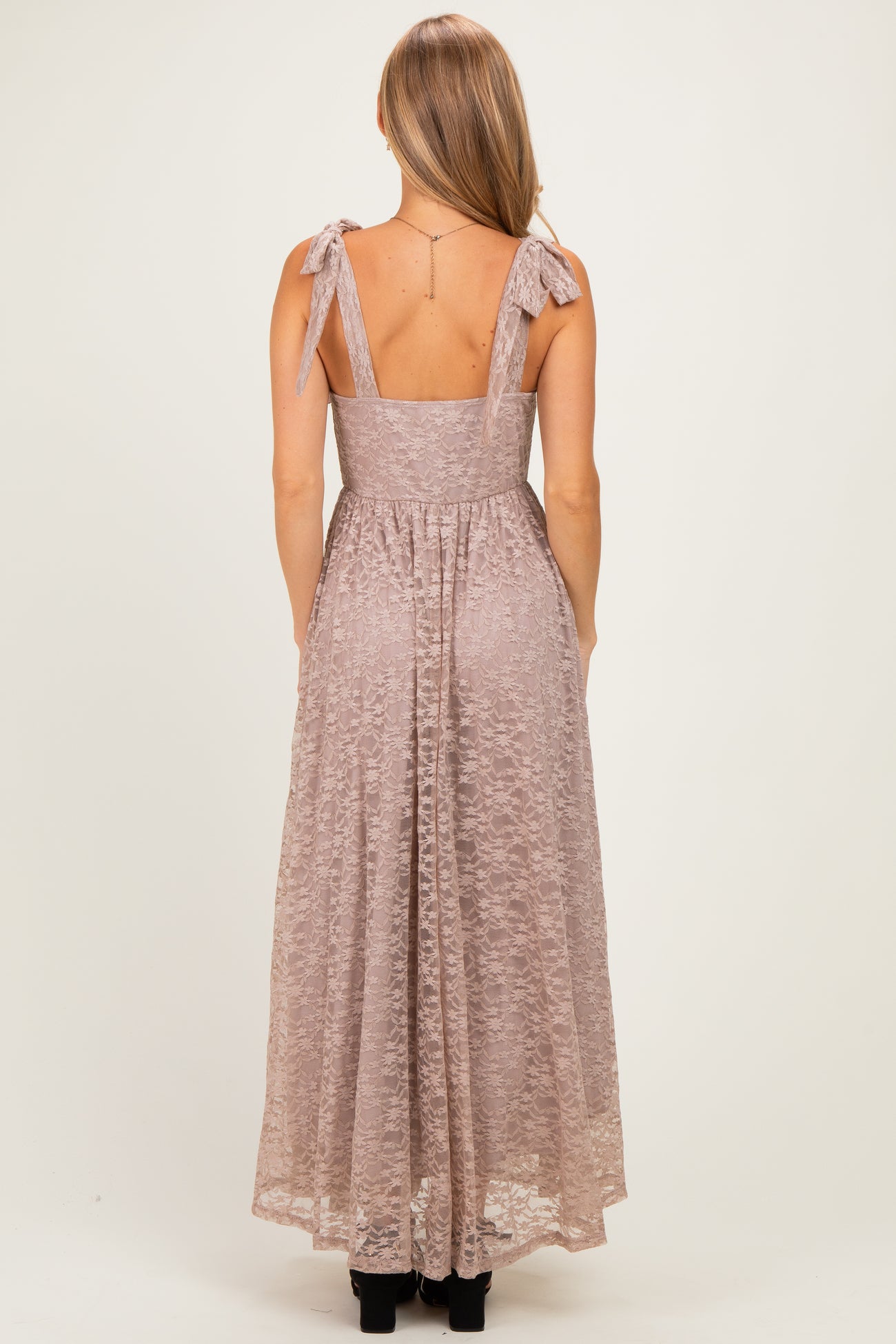 woman wearing a back view of a blush pink lace maxi dress with bow tie straps