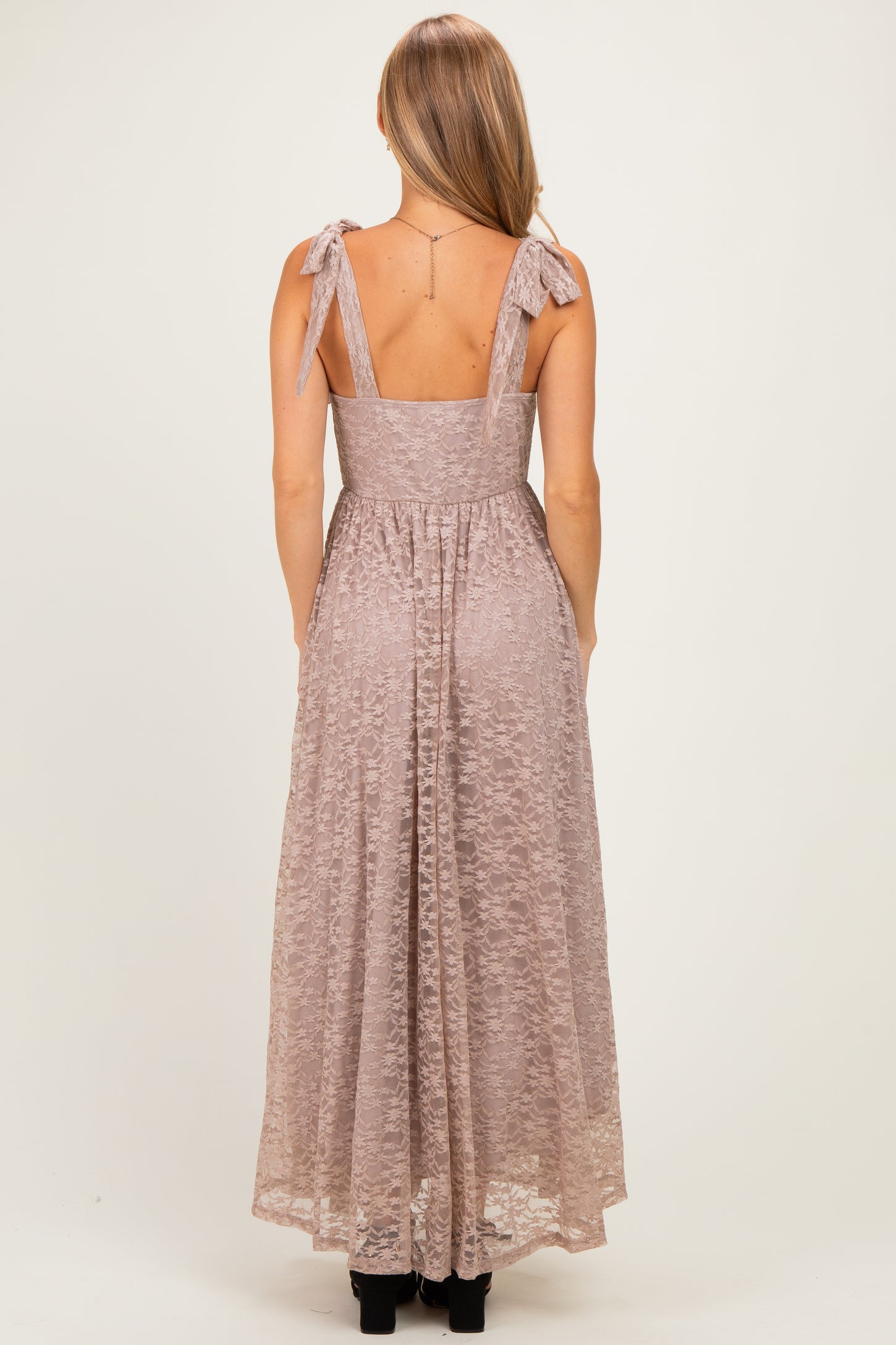 woman wearing a back view of a blush pink lace maxi dress with bow tie straps