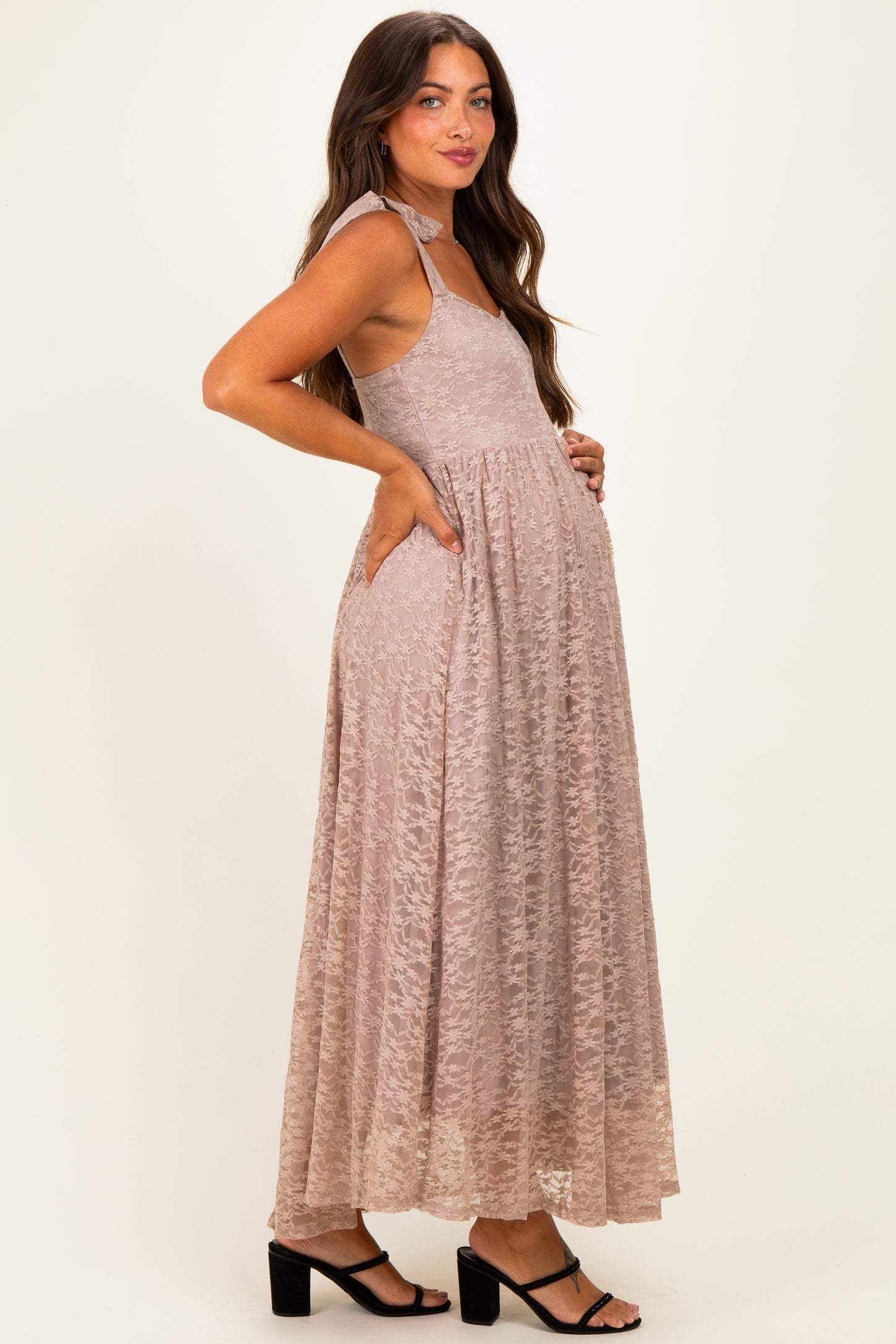 woman wearing a mauve lace maxi maternity dress with a baby bump, posing with hands in pockets