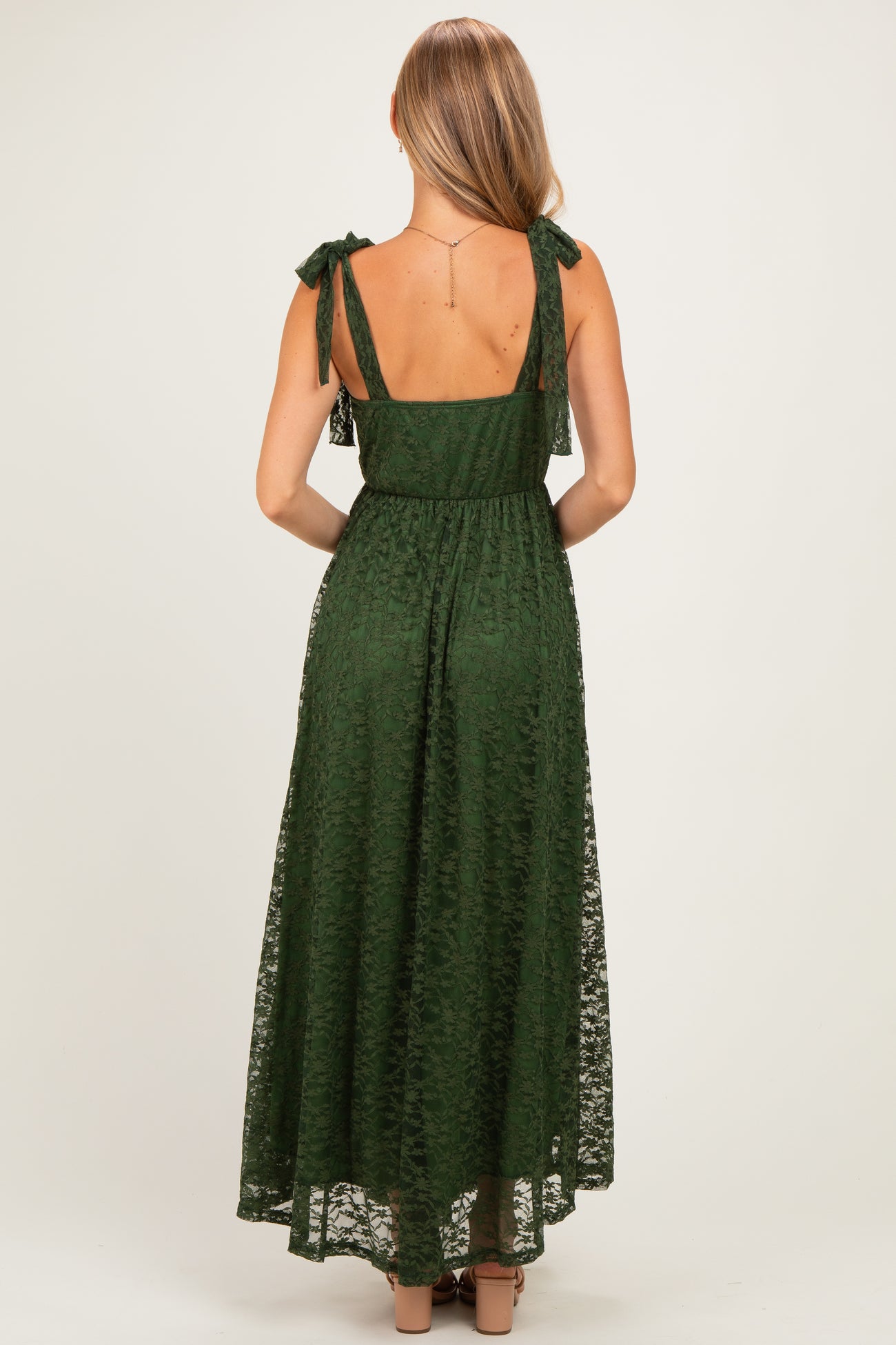 woman wearing a dark green maxi dress with tie straps and semi-sheer lace overlay, shown from the back